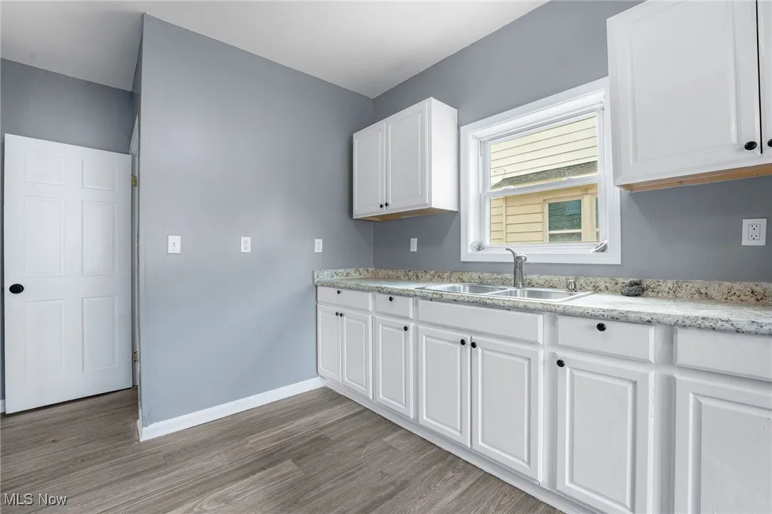 Kitchen with white cabinets, light wood-style flooring, and light stone counters