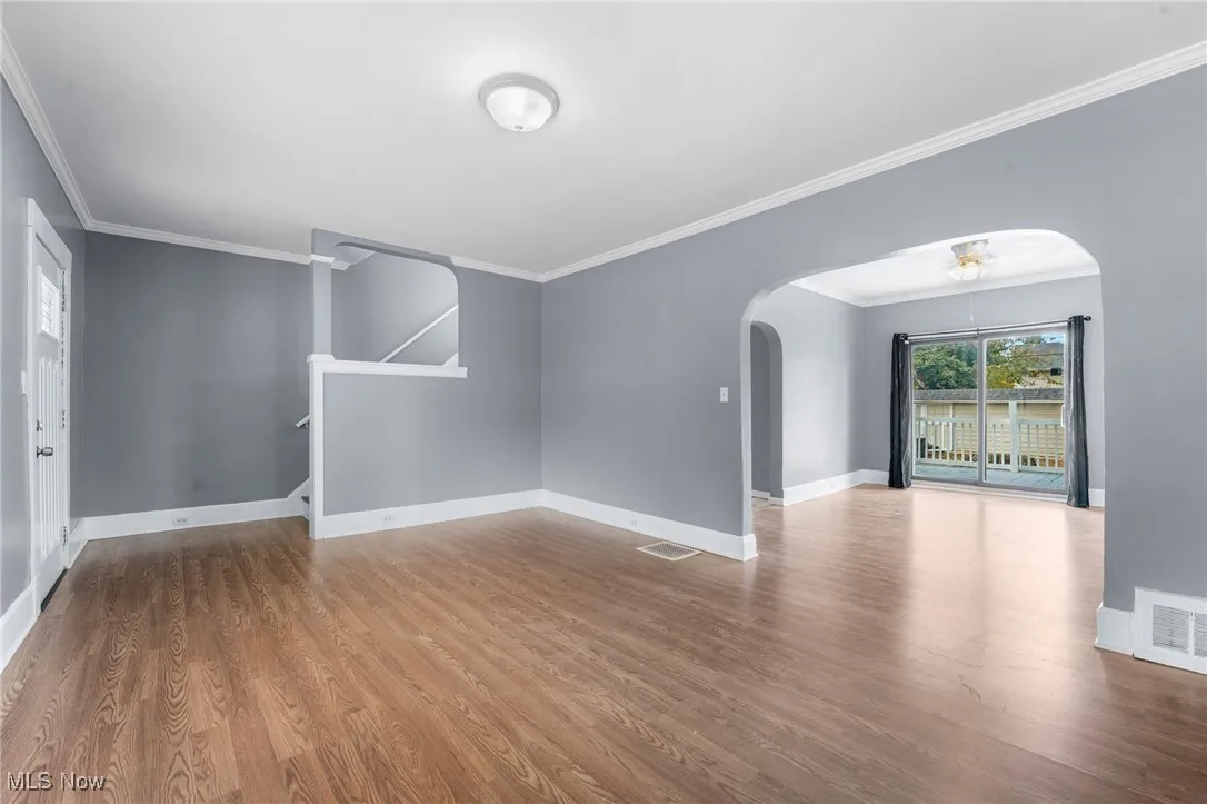 Empty room featuring crown molding, arched walkways, and light wood-style flooring