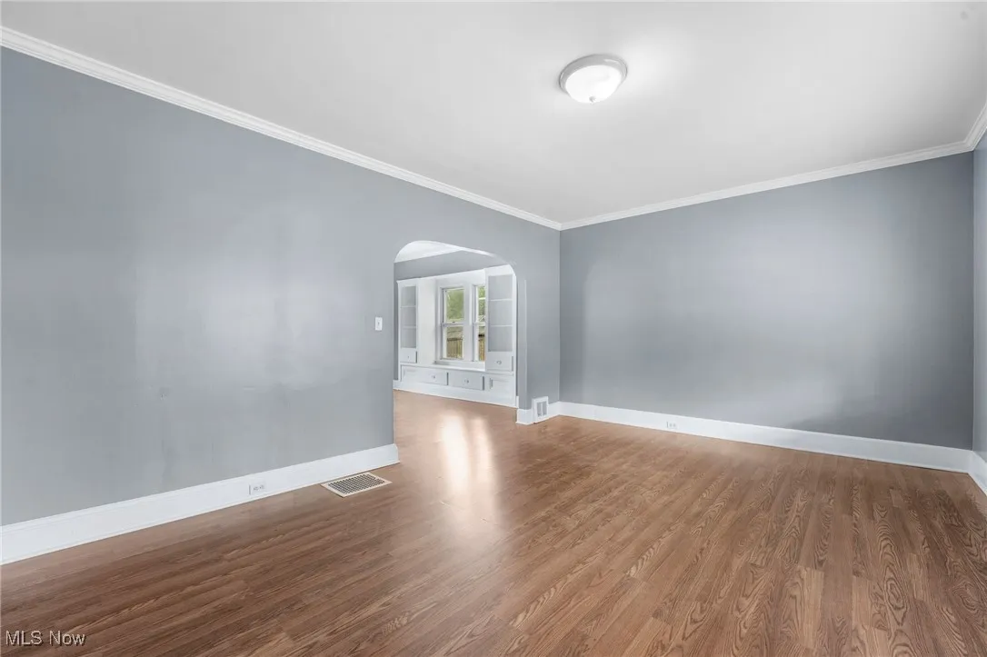Empty room with crown molding, arched walkways, and wood finished floors