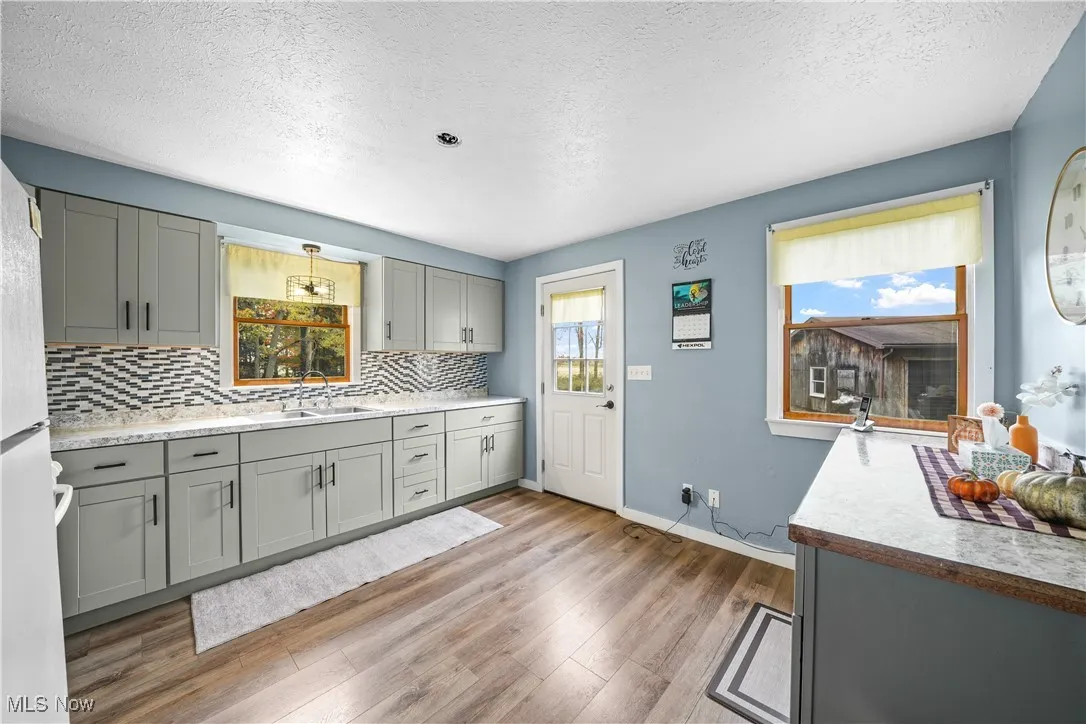 Kitchen featuring gray cabinets, a textured ceiling, light countertops, freestanding refrigerator, and light wood finished floors
