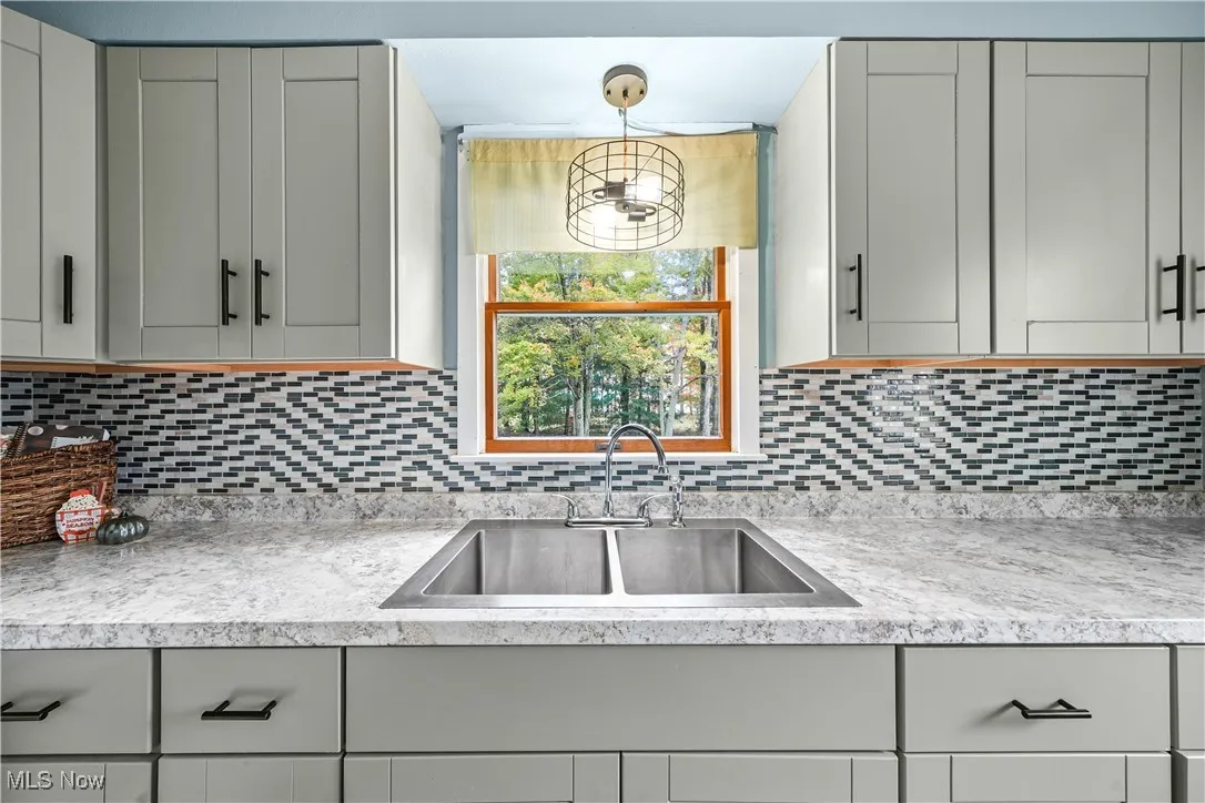 Kitchen with gray cabinets, decorative backsplash, and decorative light fixtures