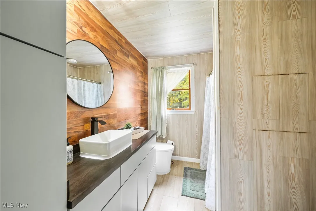 Bathroom featuring vanity, wood walls, a shower with shower curtain, light wood-style flooring, and wood ceiling