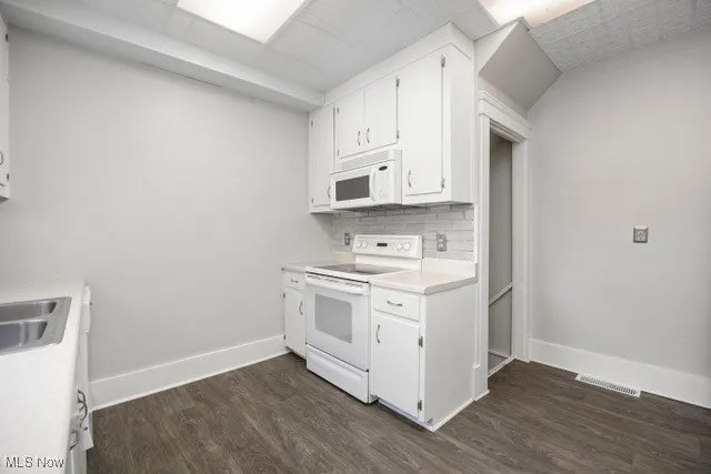 Kitchen featuring white appliances, white cabinetry, light countertops, dark wood-style flooring, and decorative backsplash