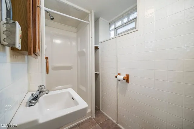 Bathroom with a shower, dark tile patterned flooring, and tile walls