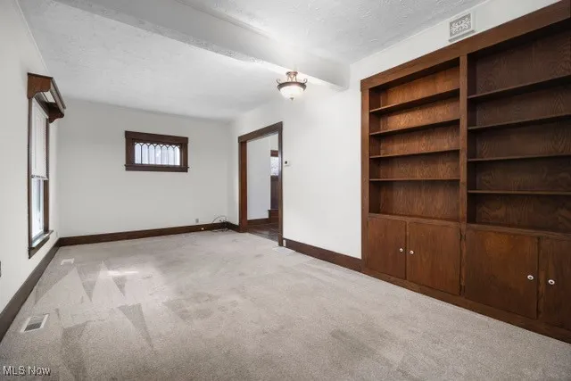 Unfurnished living room featuring light carpet, a textured ceiling, and beam ceiling