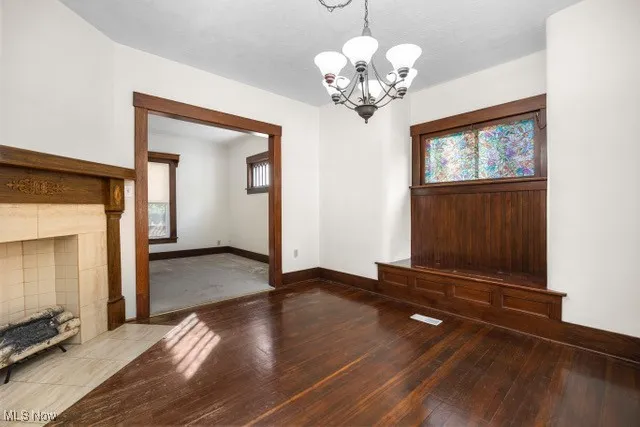Unfurnished living room featuring healthy amount of natural light, a chandelier, hardwood / wood-style flooring, and a tile fireplace