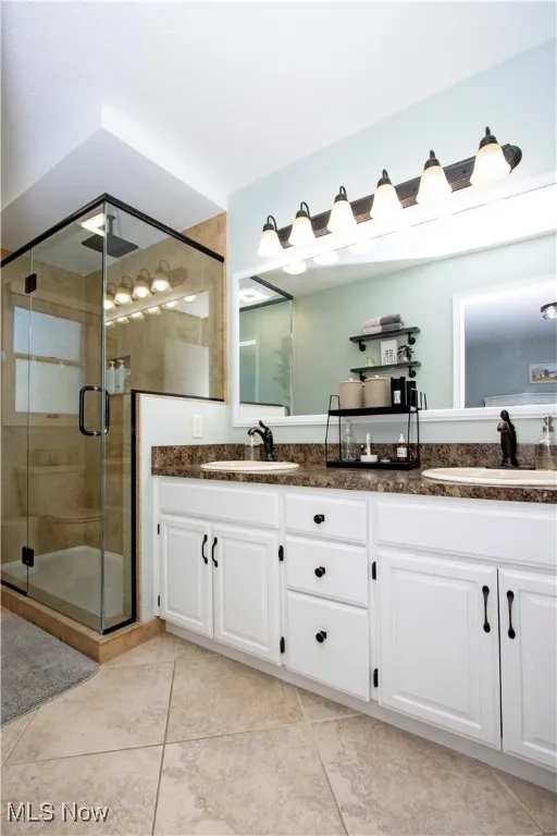 Bathroom featuring double vanity, light tile patterned floors, and a stall shower