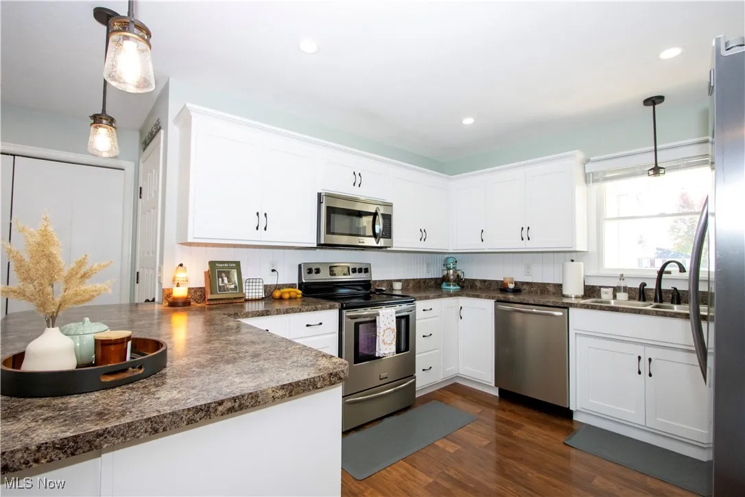 Kitchen featuring decorative light fixtures, appliances with stainless steel finishes, dark countertops, white cabinets, and recessed lighting