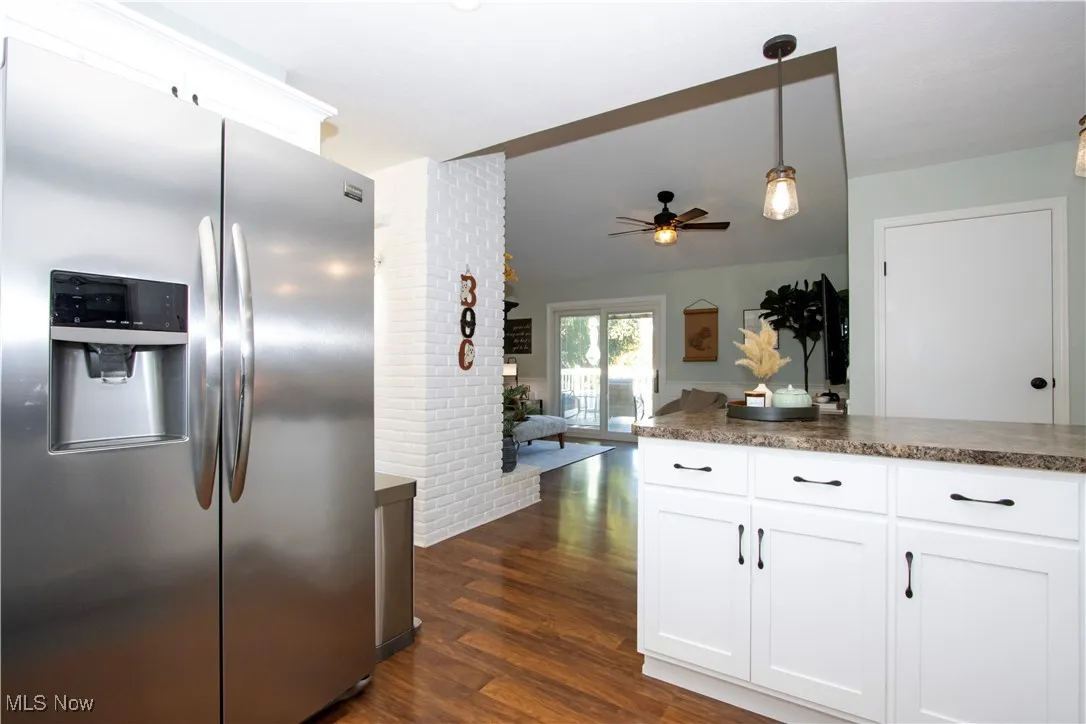 Kitchen featuring stainless steel fridge with ice dispenser, white cabinetry, dark wood-type flooring, decorative light fixtures, and brick wall
