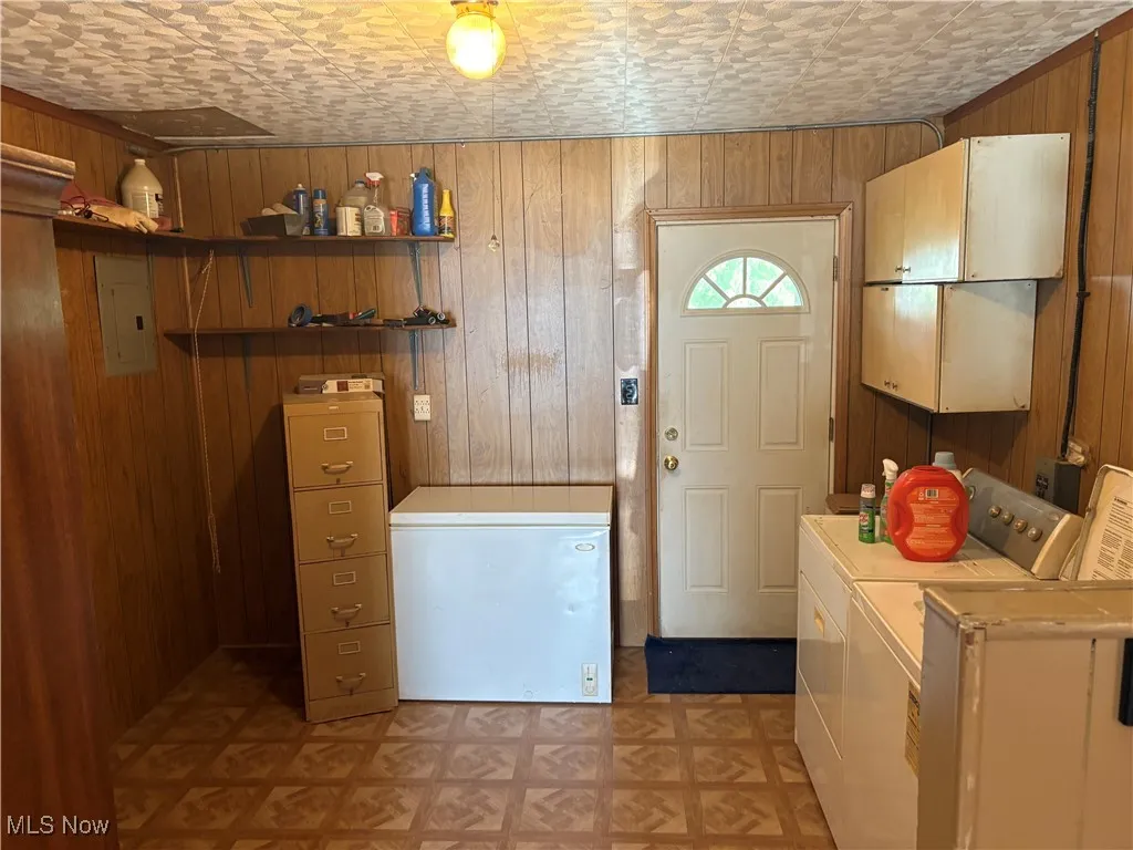 Laundry room featuring wood walls, electric panel, separate washer and dryer, and light floors