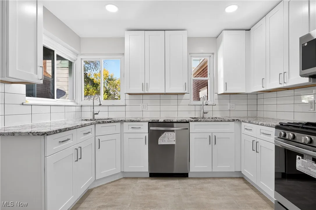 Kitchen featuring light stone counters, appliances with stainless steel finishes, decorative backsplash, white cabinets, and recessed lighting