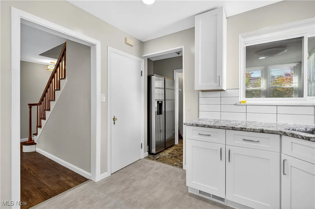 Kitchen featuring stainless steel refrigerator with ice dispenser, white cabinets, light stone countertops, and decorative backsplash
