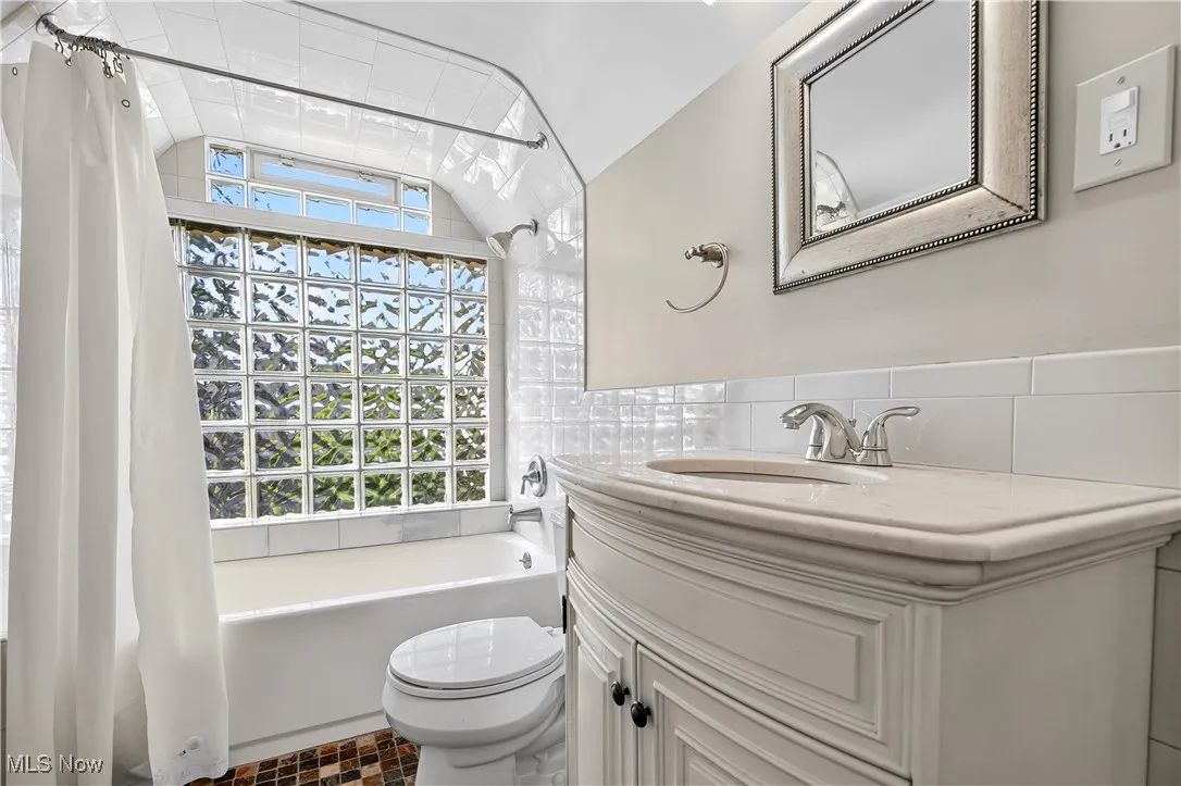 Full bath with shower / bathtub combination with curtain, vanity, tile walls, and dark tile patterned flooring