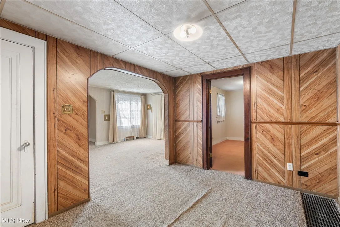 Corridor with arched walkways, wooden walls, light colored carpet, and a paneled ceiling