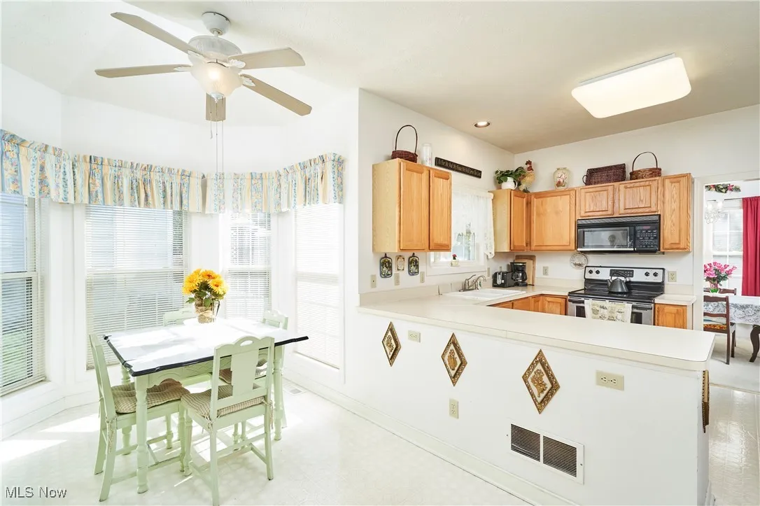 Kitchen featuring light countertops, electric stove, light flooring, black microwave, and ceiling fan