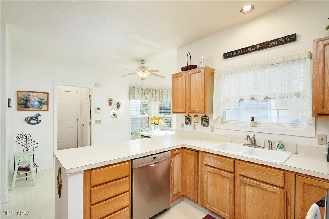 Kitchen with light countertops, dishwasher, a peninsula, a ceiling fan, and light flooring