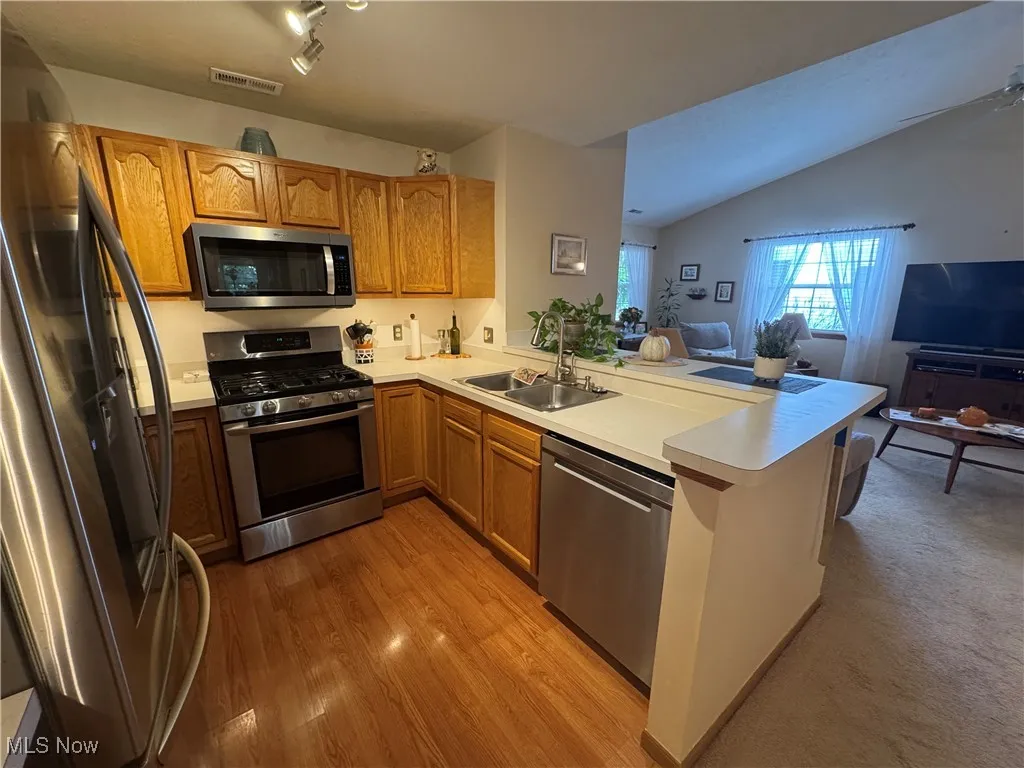 Kitchen featuring open floor plan, stainless steel appliances, light countertops, and oak cabinetry