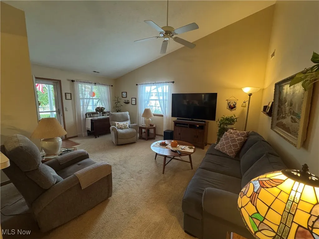 Carpeted living room featuring high vaulted ceiling and a ceiling fan