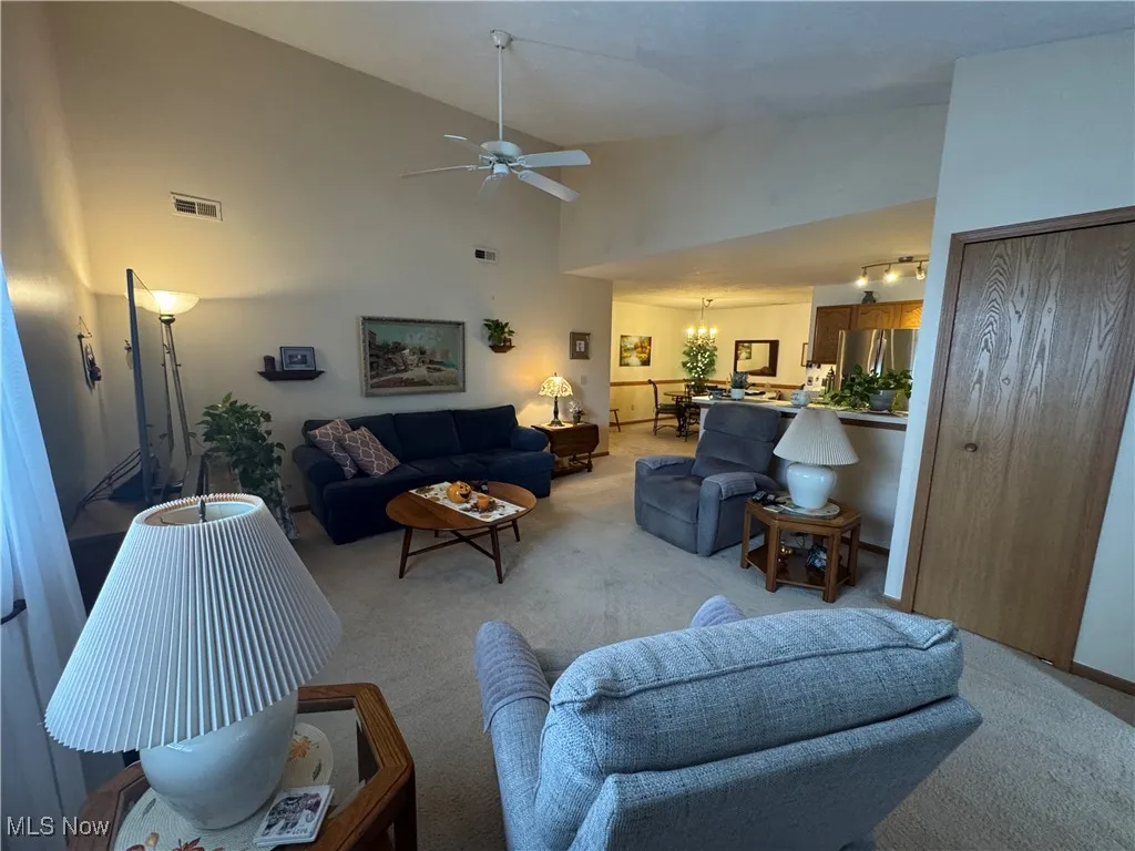 Carpeted living area with high vaulted ceiling, a ceiling fan, and guest closet