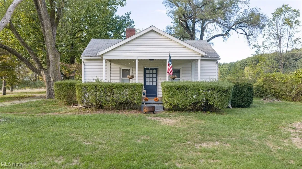Bungalow-style house with a front lawn, covered porch, a chimney, and roof with shingles