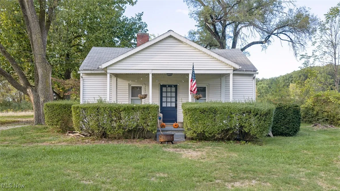 Bungalow-style house with a front lawn, covered porch, a chimney, and roof with shingles
