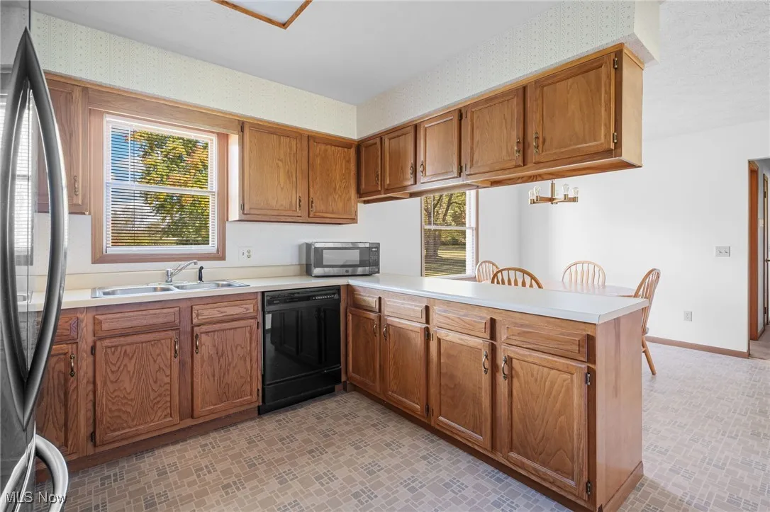 Kitchen with light countertops, appliances with stainless steel finishes, a peninsula, brown cabinets, and wallpapered walls