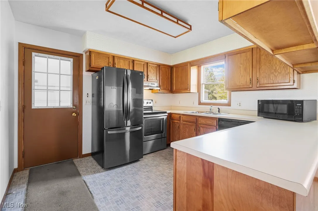 Kitchen with brown cabinets, black appliances, light countertops, a peninsula, and under cabinet range hood