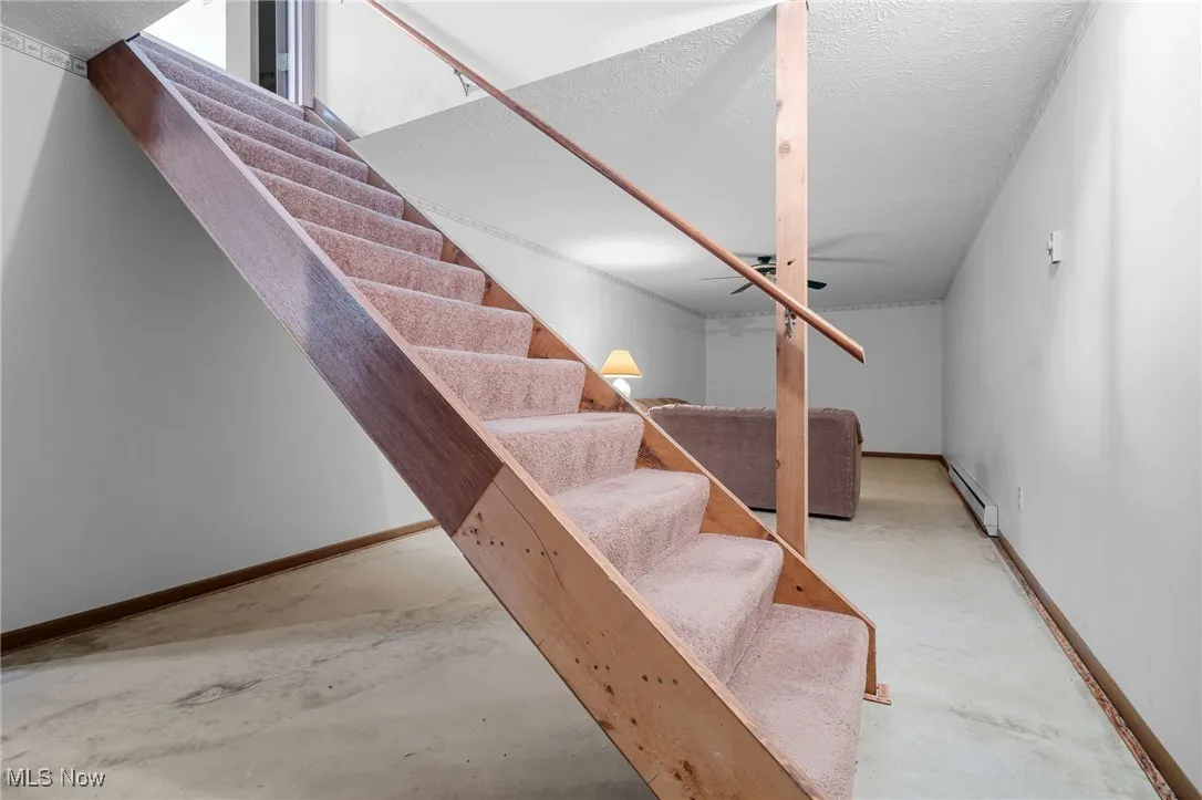Stairway with a textured ceiling, unfinished concrete flooring, and a baseboard heating unit