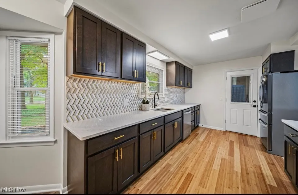 Kitchen featuring decorative backsplash, stainless steel appliances, light wood-style flooring, and light stone counters
