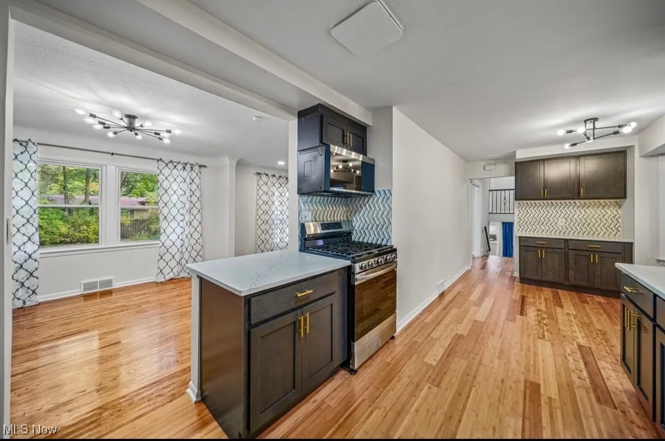 Kitchen featuring a chandelier, stainless steel appliances, decorative backsplash, light wood-style flooring, and light stone countertops