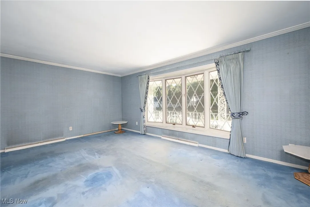 Unfurnished room with crown molding, baseboard heating, and wallpapered walls