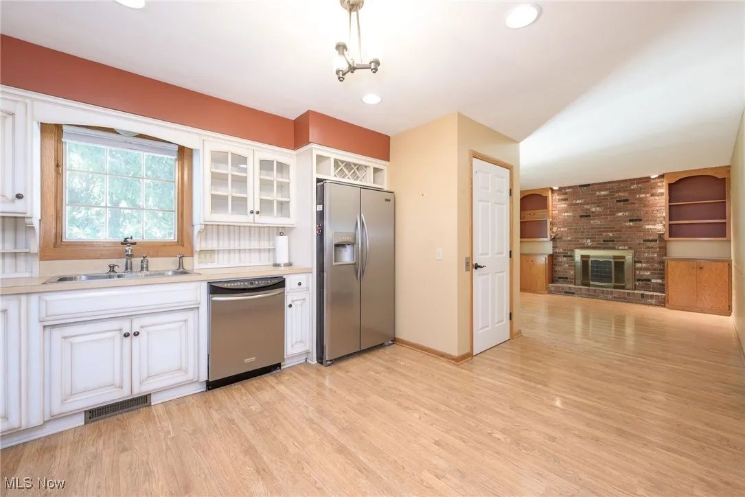 Kitchen featuring stainless steel appliances, white cabinetry, light countertops, light wood-style floors, and glass insert cabinets