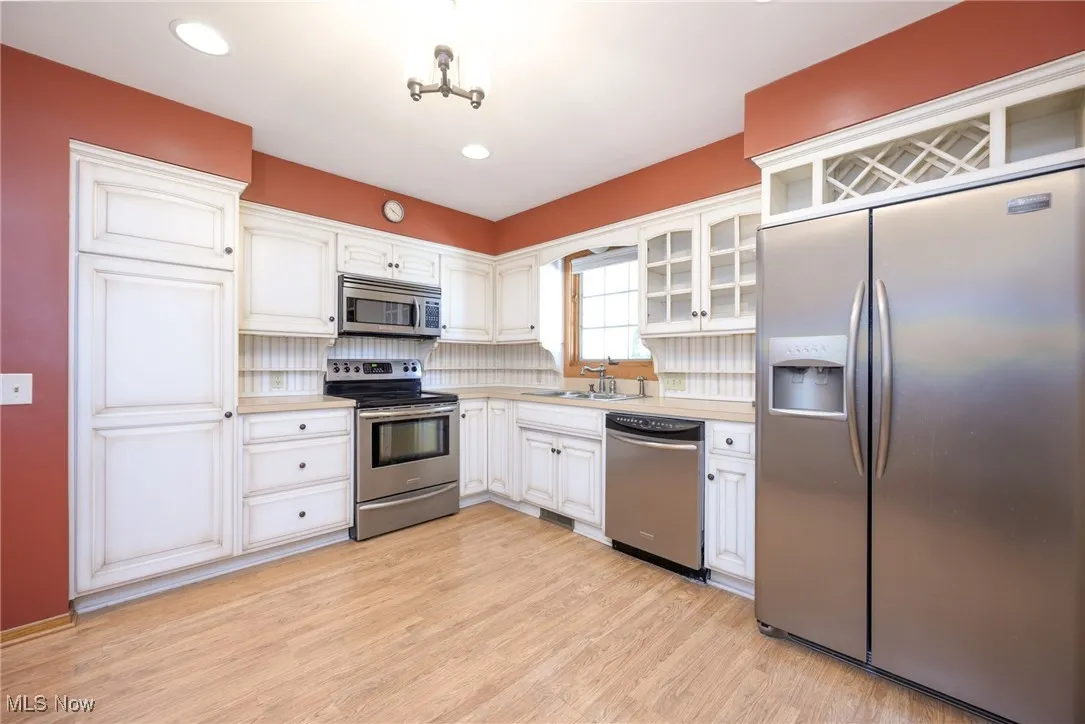 Kitchen featuring stainless steel appliances, light countertops, light wood-type flooring, glass insert cabinets, and white cabinetry