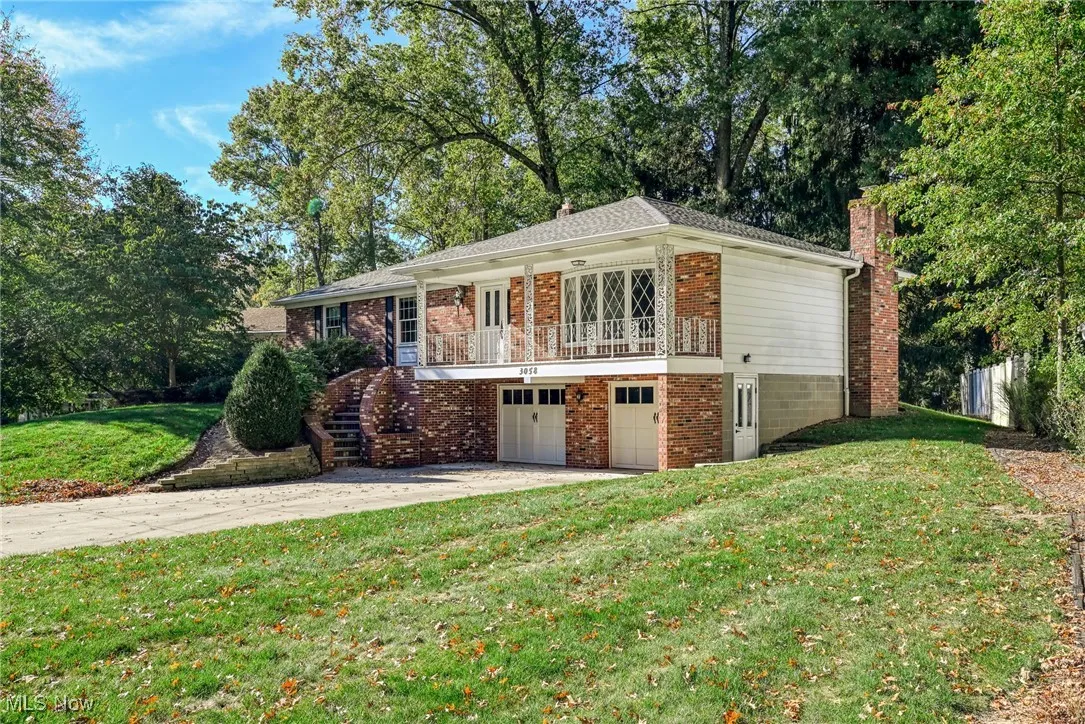 View of front of property featuring a balcony, stairs, a front lawn, brick siding, and concrete driveway