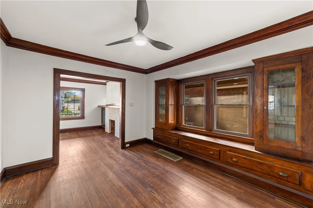 Spare room featuring crown molding, dark wood-type flooring, a fireplace, and ceiling fan