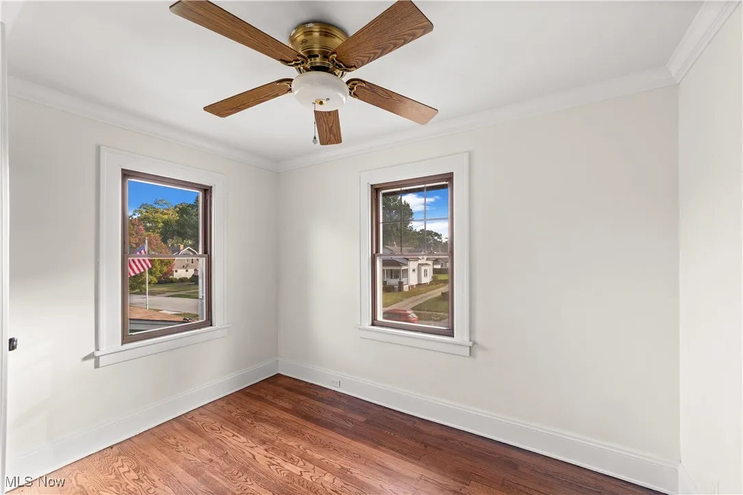 Empty room with crown molding, wood finished floors, and ceiling fan