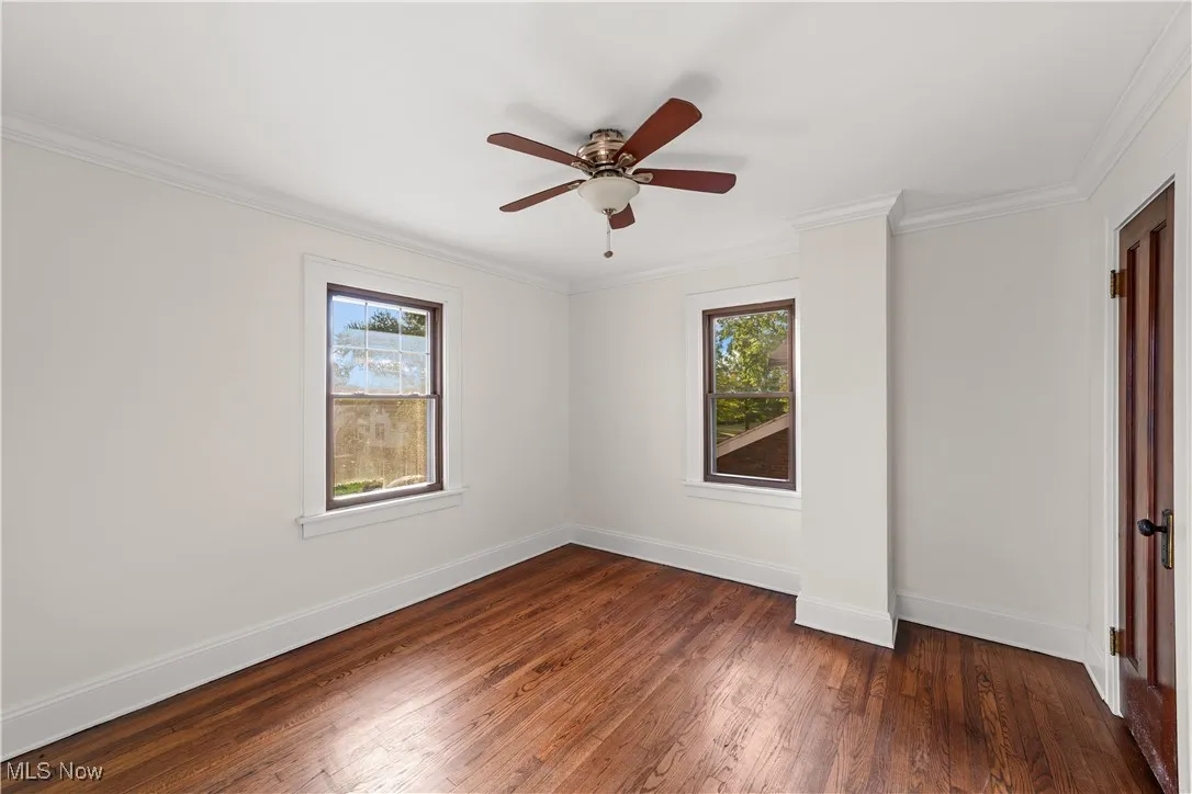 Spare room with dark wood-type flooring, ornamental molding, and a ceiling fan
