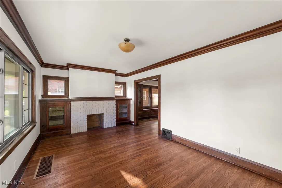 Unfurnished living room with dark wood finished floors, ornamental molding, and a fireplace
