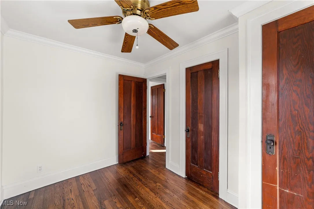Unfurnished bedroom featuring ornamental molding, dark wood-style floors, and ceiling fan
