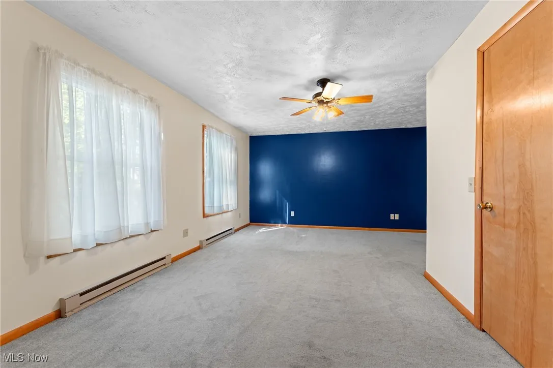 Spare room featuring a baseboard heating unit, a textured ceiling, carpet floors, and ceiling fan