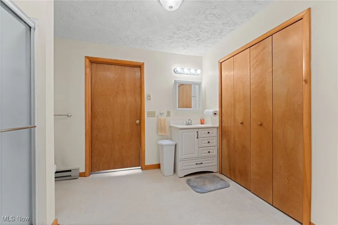Full bath featuring vanity, a textured ceiling, a shower stall, and a baseboard heating unit