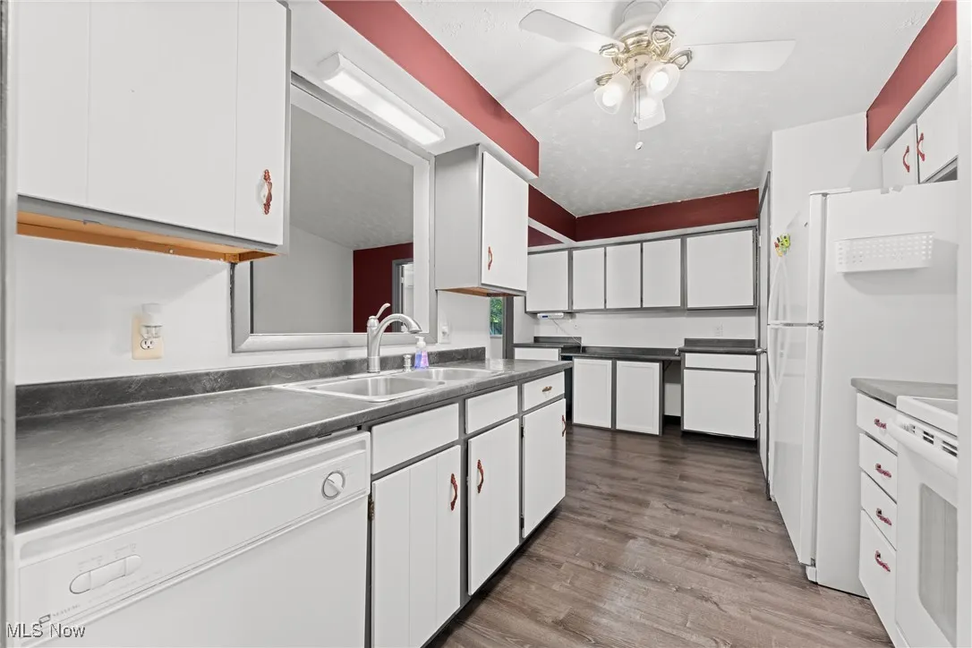 Kitchen with white cabinets, white appliances, dark wood-style flooring, ceiling fan, and dark countertops