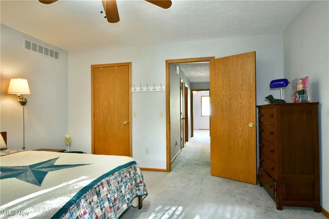 Bedroom with light carpet, a ceiling fan, and a textured ceiling