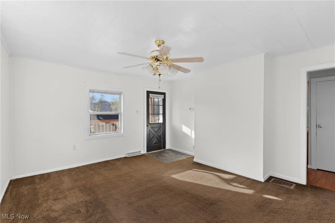 Spare room with dark carpet, a ceiling fan, and ornamental molding