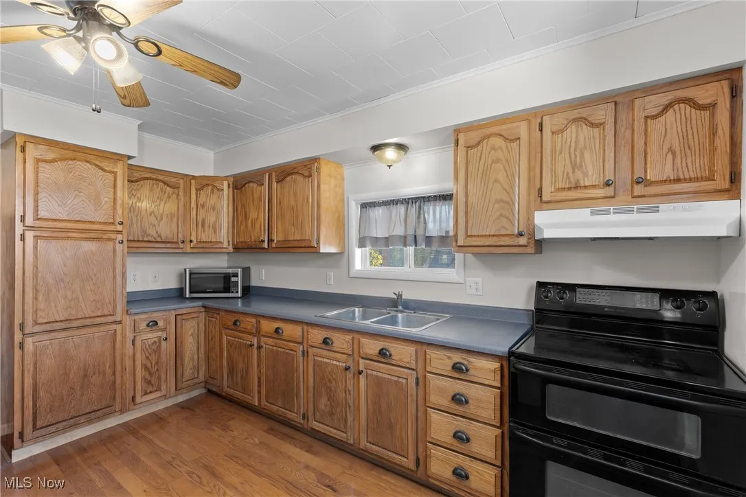 Kitchen featuring black range with electric cooktop, dark countertops, wood finished floors, under cabinet range hood, and ceiling fan