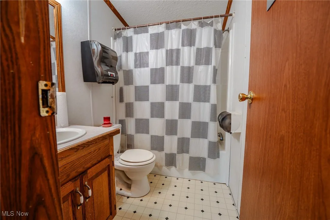 Bathroom featuring a textured ceiling, vanity, and shower / tub combo with curtain