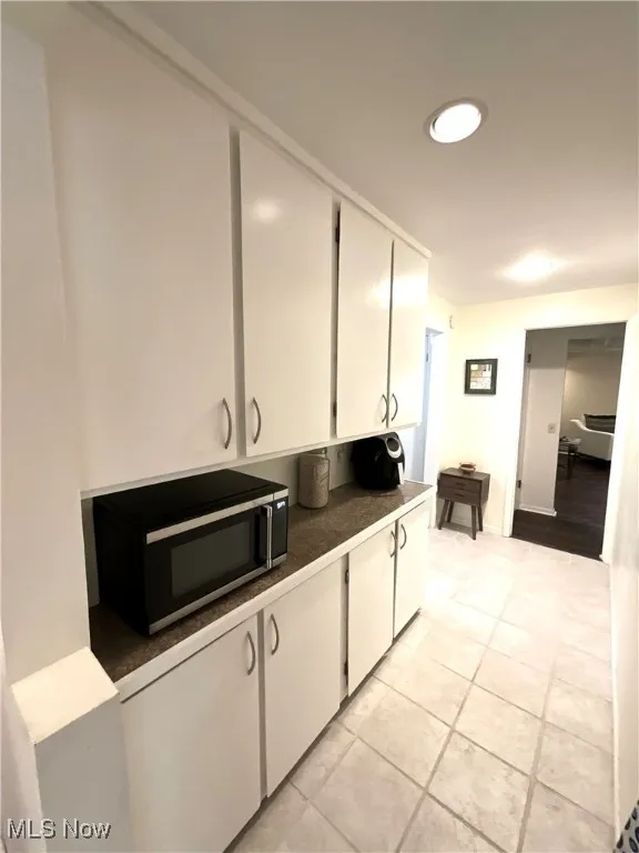 Kitchen featuring white cabinetry, stainless steel microwave, dark countertops, light tile patterned floors, and recessed lighting