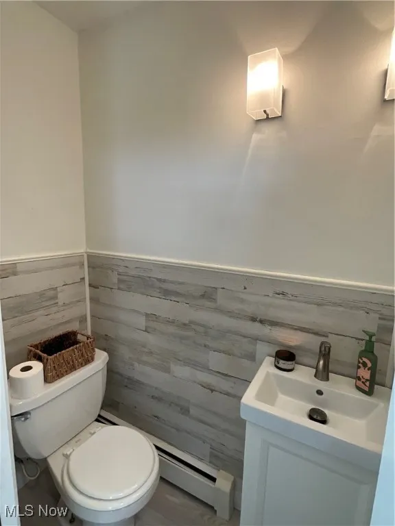 Half bathroom with a wainscoted wall, vanity, and a baseboard radiator