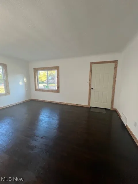 Empty room featuring baseboards and dark wood finished floors