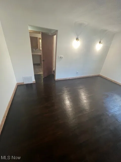 Unfurnished room featuring baseboards and dark wood-style flooring